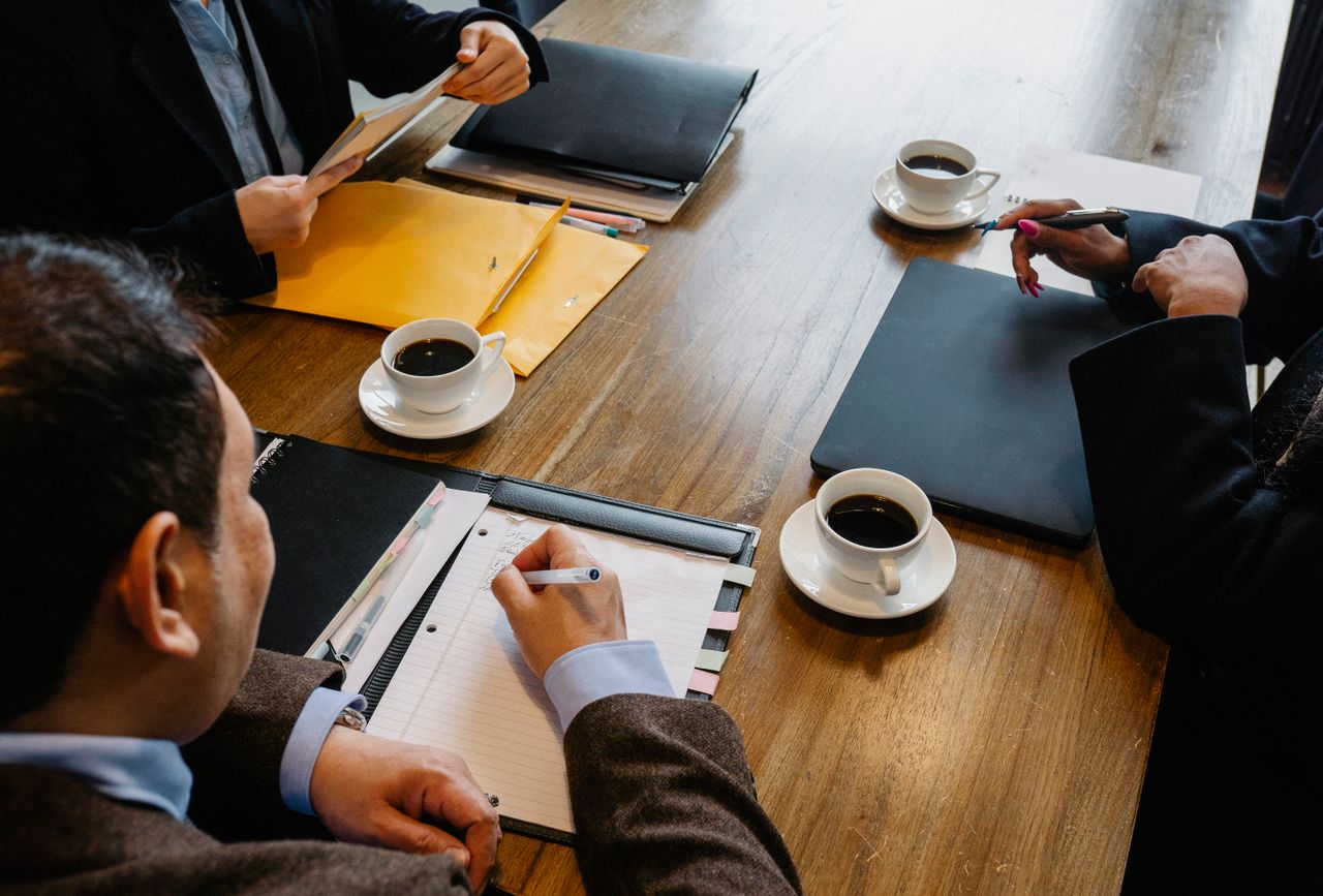 High angle of crop anonymous diverse coworkers sitting at table with documents and coffee while discussing business issues